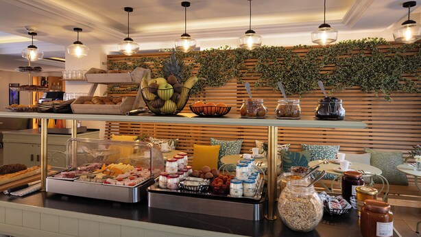 A buffet area with various food items, including fruits, pastries, and breakfast foods, arranged on a counter with a glass display case.