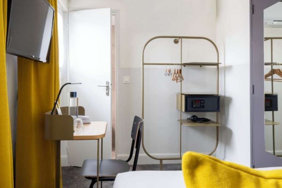 Una camera d'albergo con un letto, una scrivania con una sedia, una televisione, un armadio e uno specchio.