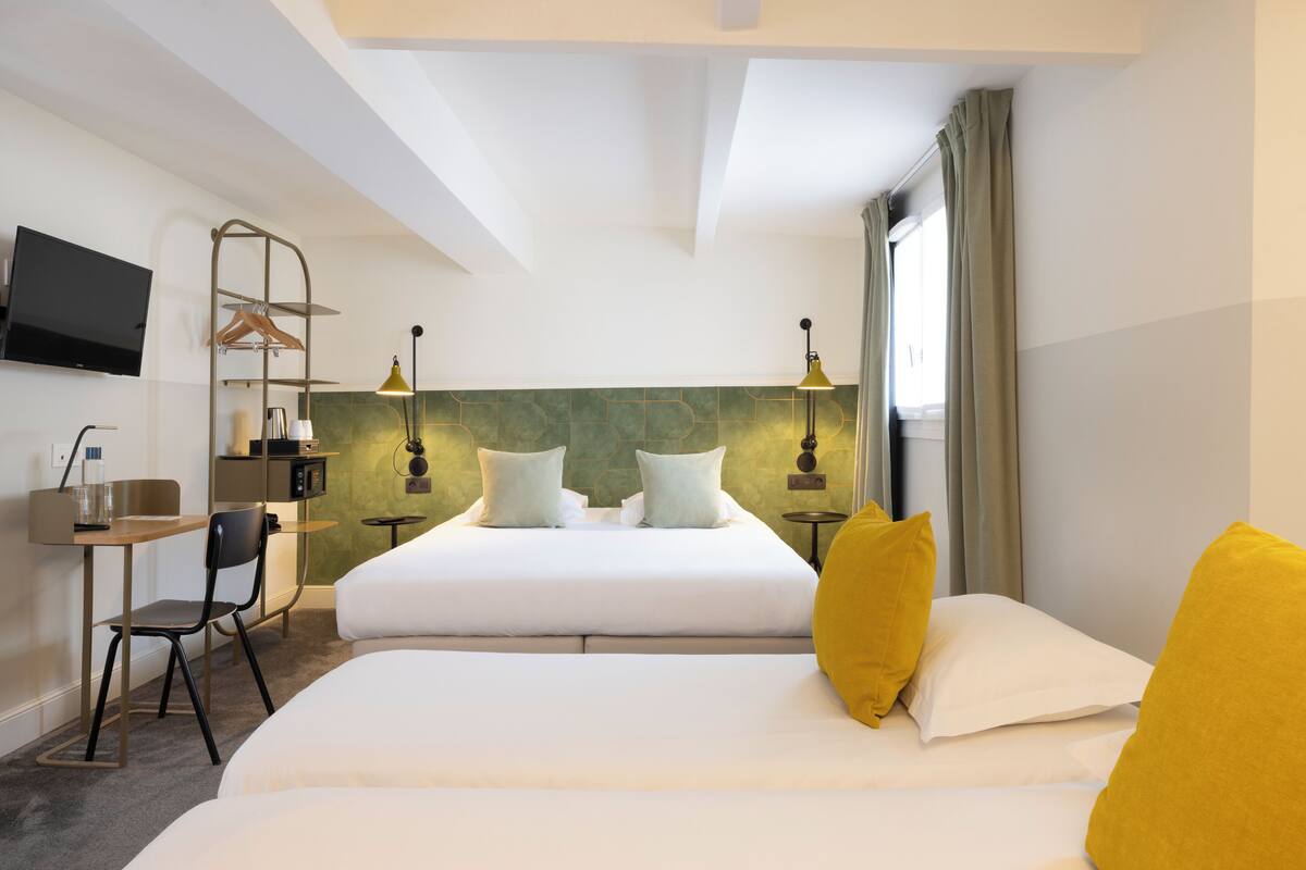 A hotel room with a bed, a desk, a chair, a TV, and a lamp.