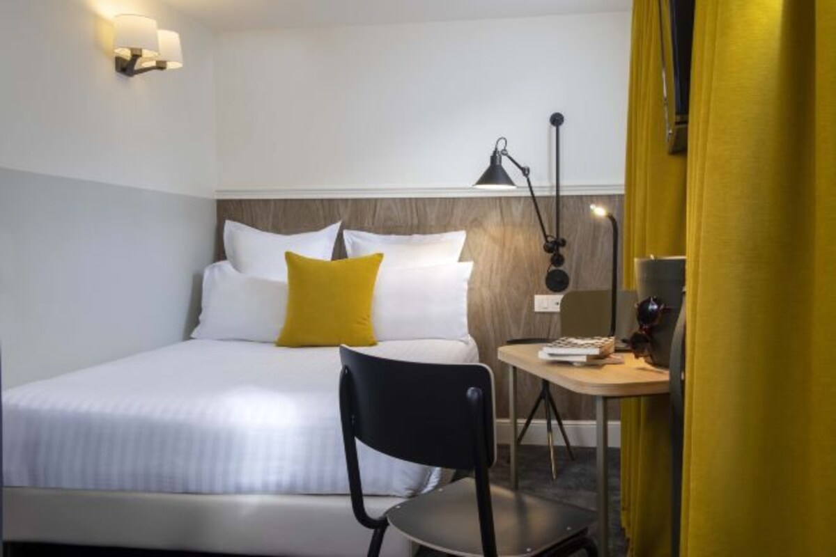A hotel room with a bed, a desk, a chair, and a lamp.