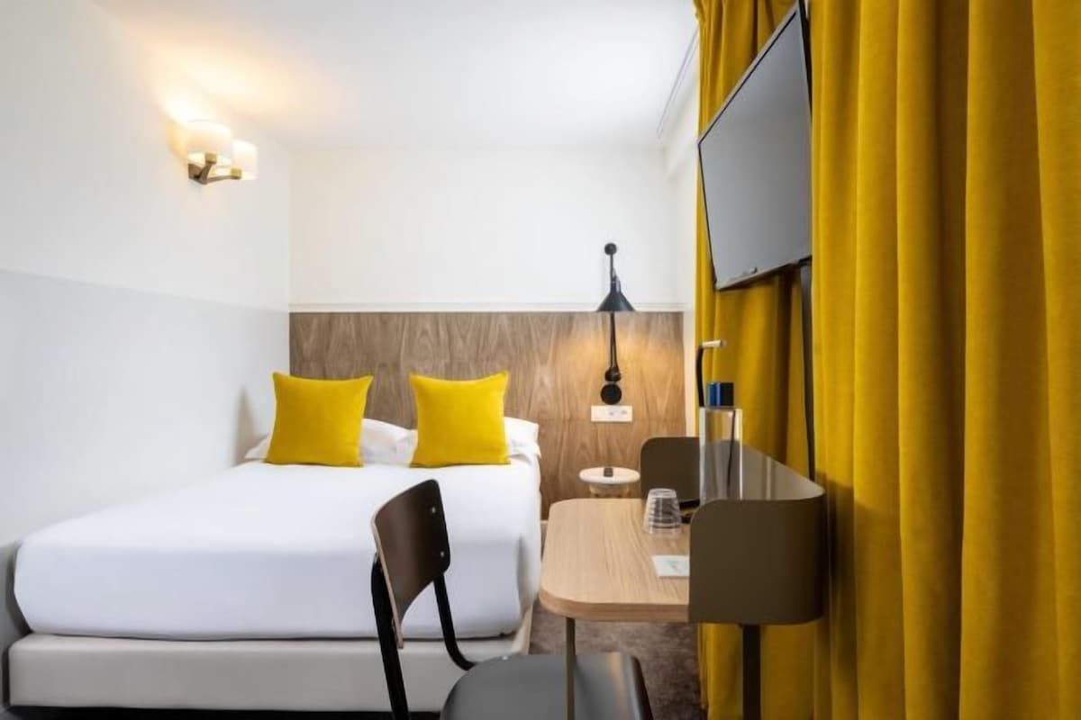 Una camera d'albergo con un letto, una scrivania, una sedia, una lampada e una TV.
