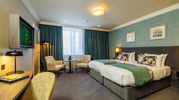 A hotel room with a large bed, two bedside tables, a desk, a chair, and a TV.