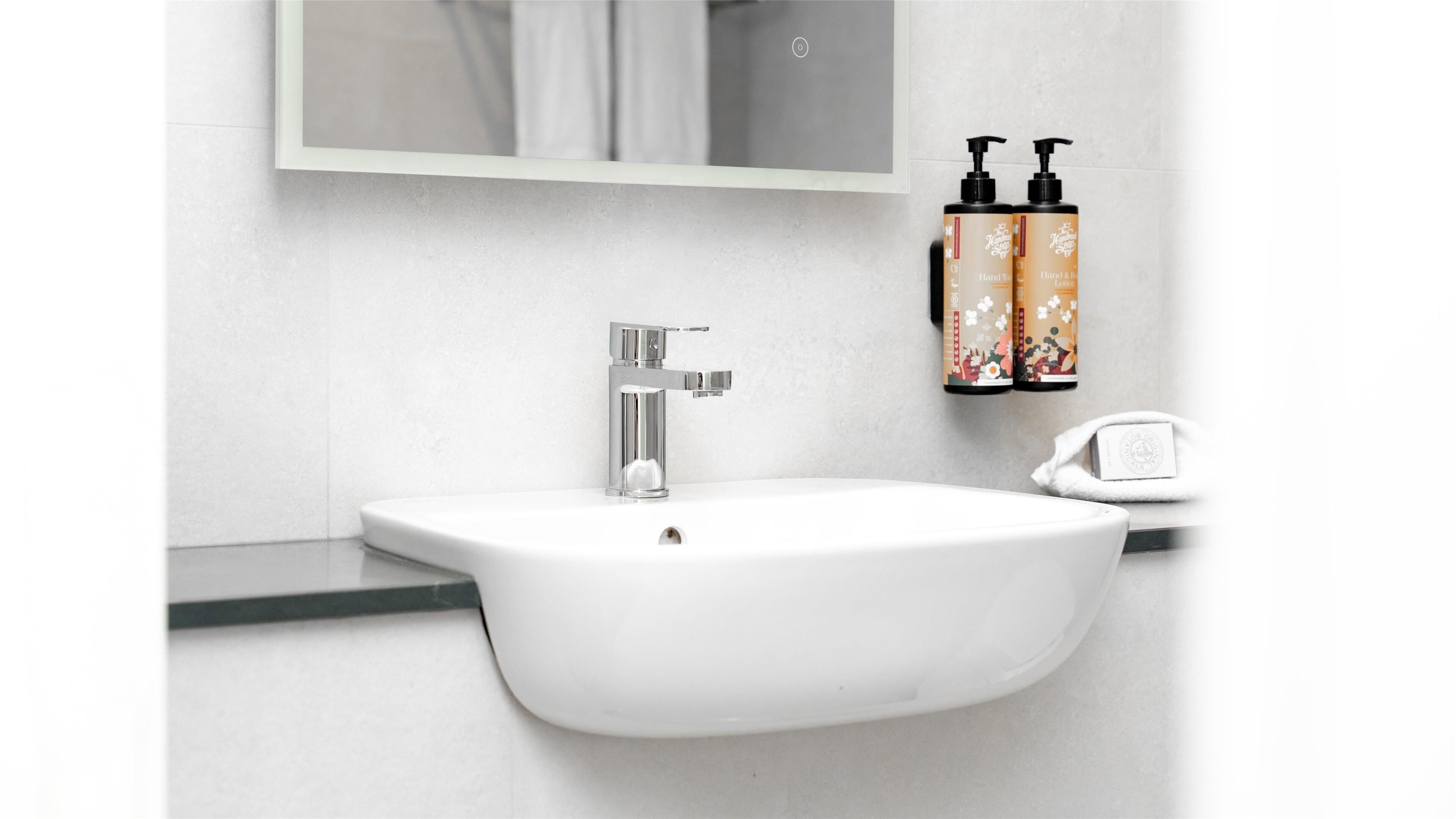 A white bathroom sink with a chrome faucet, a mirror above it, and two toiletry bottles on the wall.