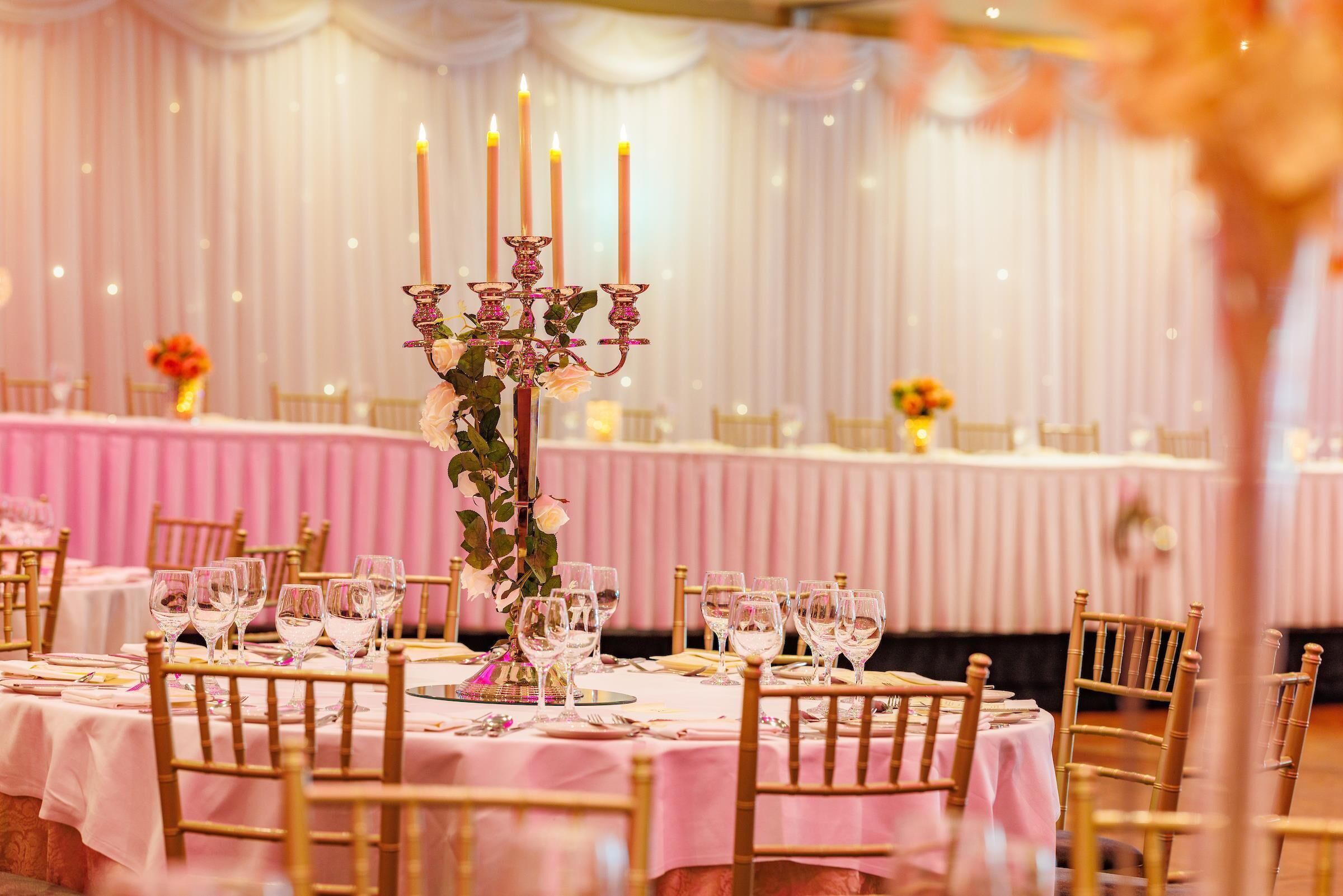 A banquet hall with round tables set for a formal event, featuring candelabras and floral centerpieces.