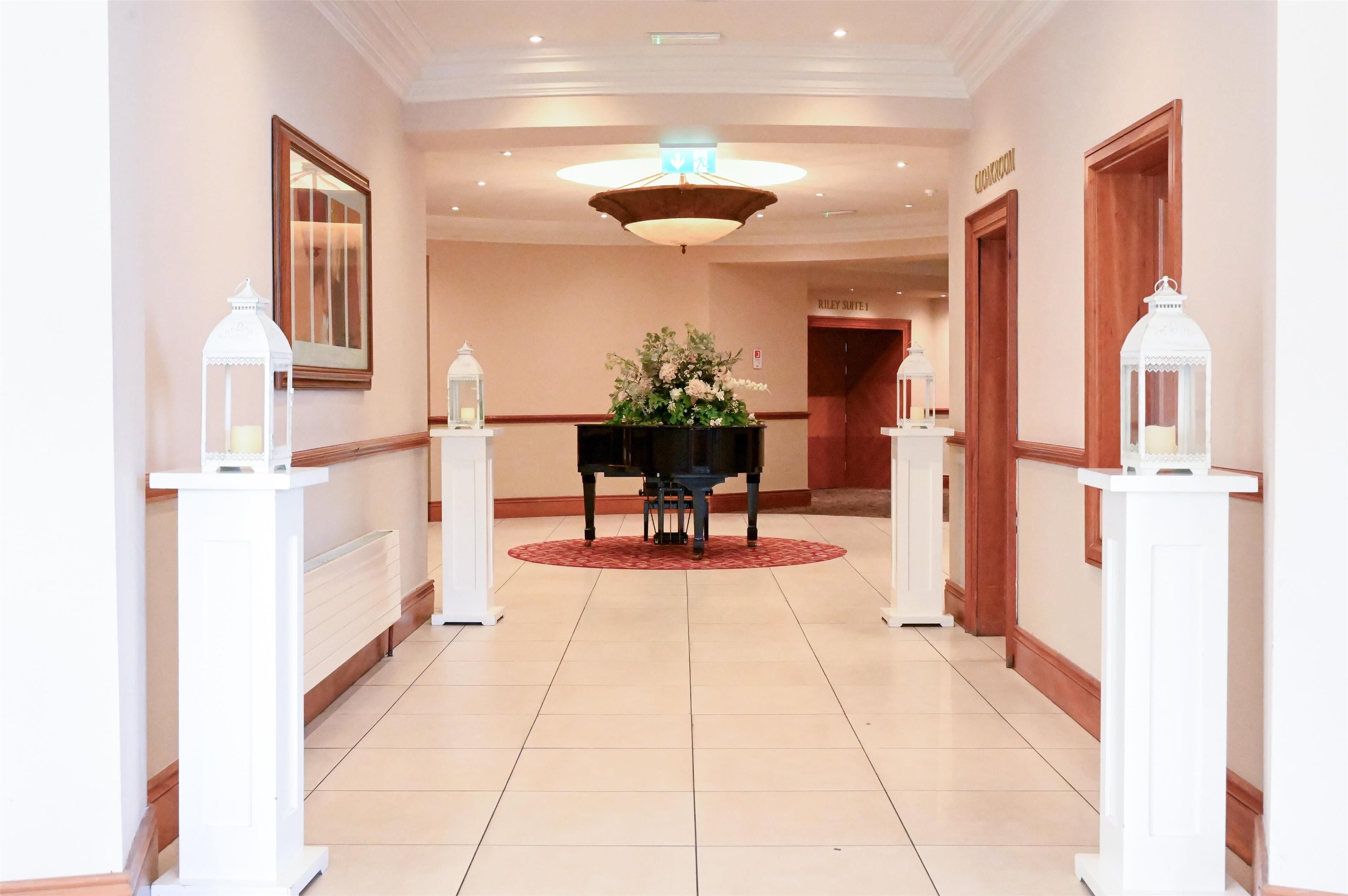 Atrio di un hotel con un pianoforte a coda, un'elaborata composizione floreale e lanterne bianche su piedistalli.