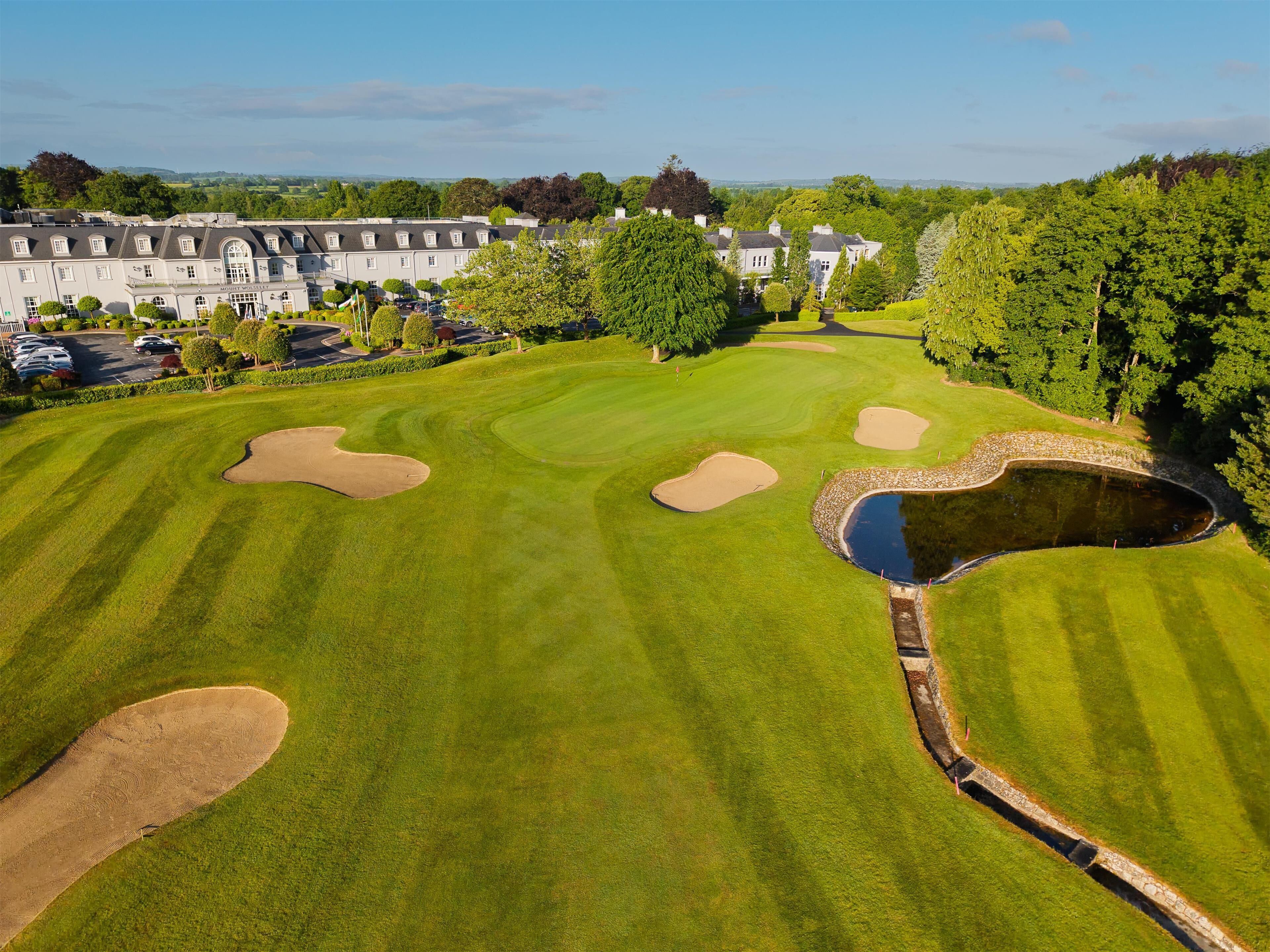Un parcours de golf avec des bunkers, un étang et un club-house en arrière-plan.