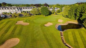 Un parcours de golf avec des bunkers, un étang et un club-house en arrière-plan.