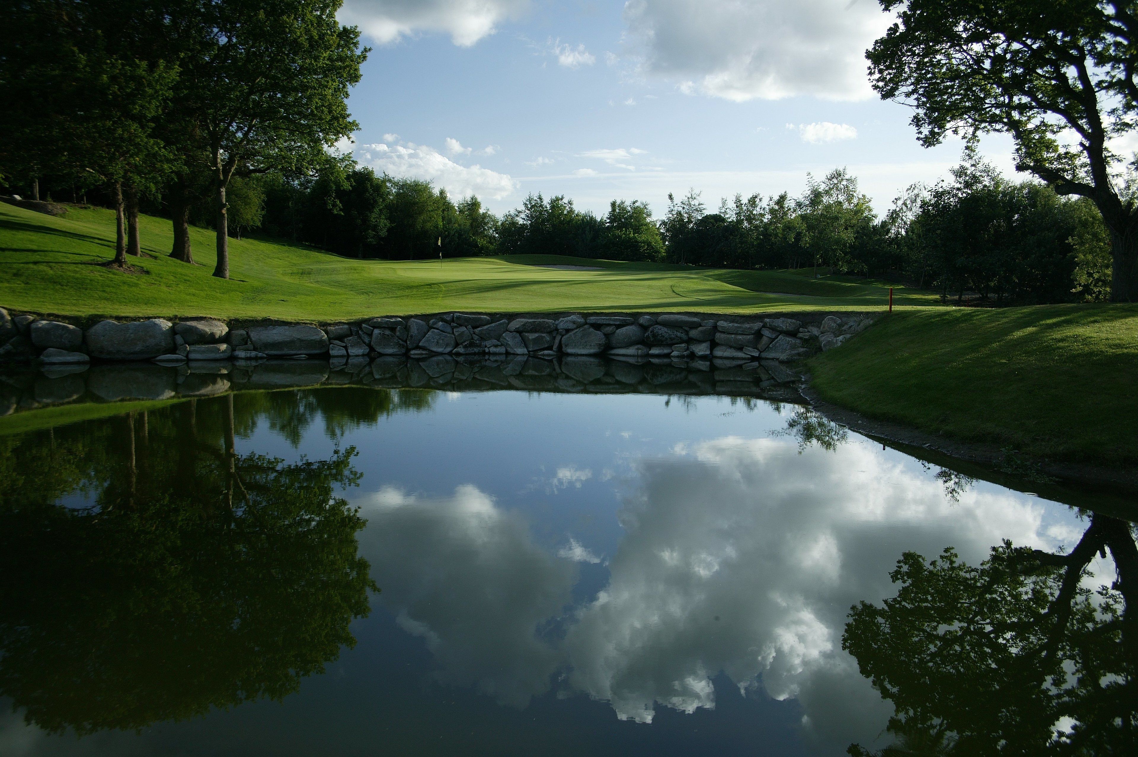 Een rustige golfbaan met een vijver die bomen en de lucht weerspiegelt.