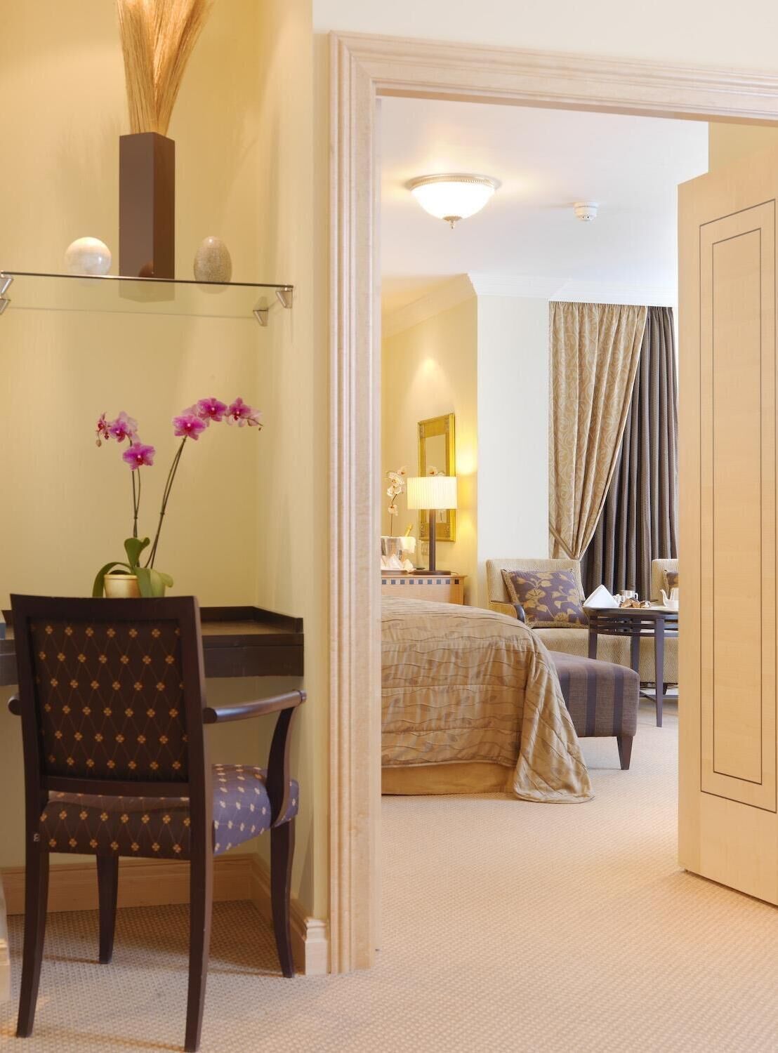 A hotel room with a desk, chair, bed, and a view of the hallway.