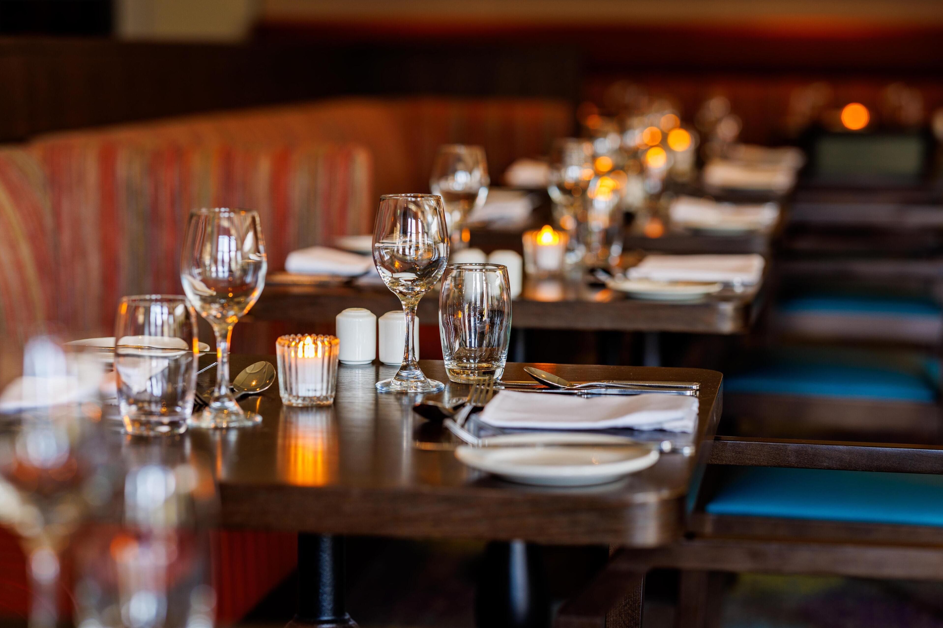 Een restaurantsetting met gedekte tafels, helder glaswerk, borden en kaarsen.