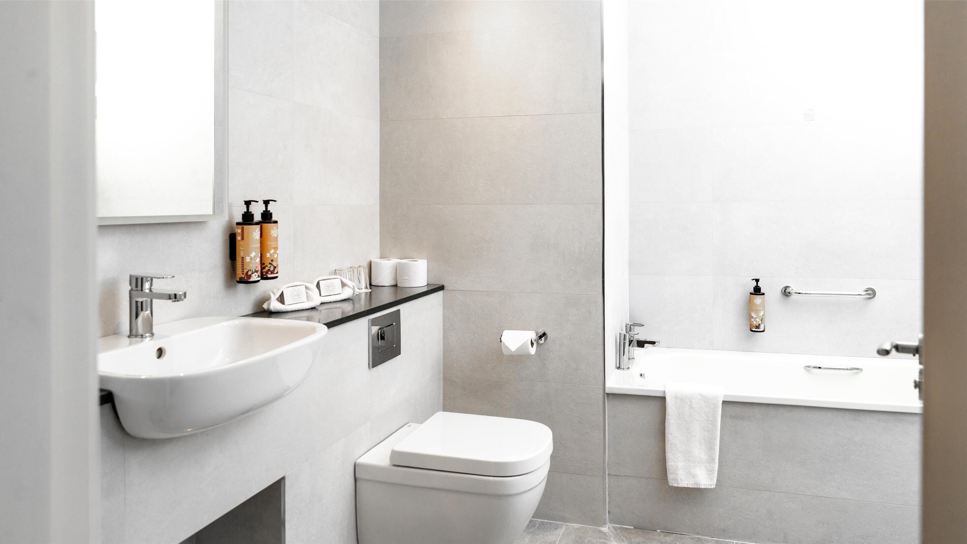 Een moderne badkamer met een wastafel, toilet en bad. Er staan toiletartikelen op de wastafel en een handdoekhouder naast het bad.