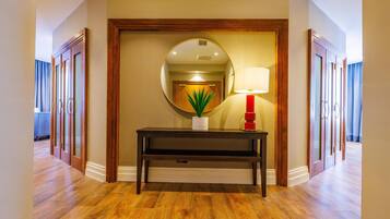 A hallway with wooden flooring, a dark console table with a potted plant, a mirror, and a red lamp.