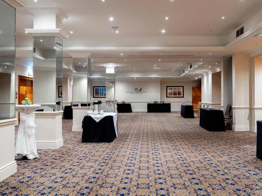 A spacious conference room with a patterned carpet, white columns, and a logo on the wall.