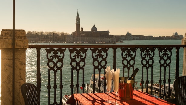 Ein Balkon mit Esstisch, Blick auf einen Fluss und historische Gebäude im Hintergrund.