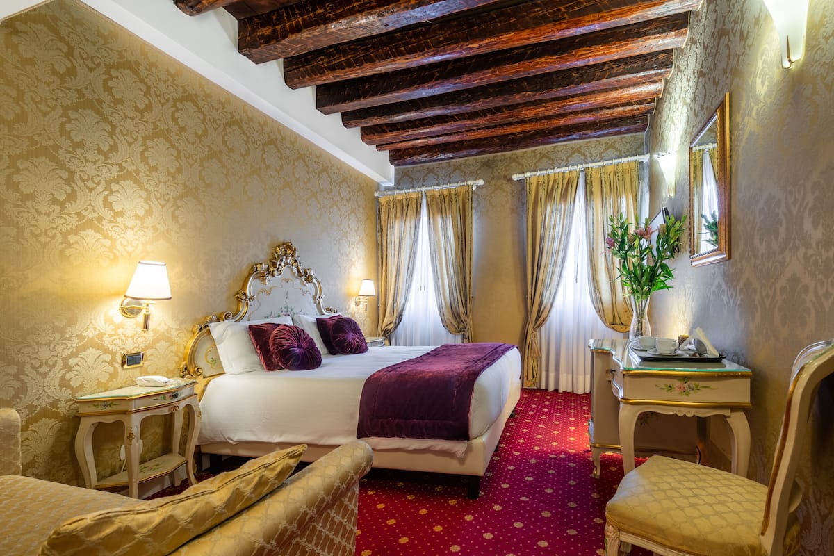 Ein Hotelzimmer mit einem großen Bett, einem Nachttisch mit Lampe, einem Sessel und einem kleinen Tisch mit Blumen.