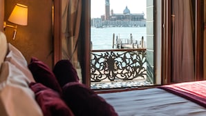 Ein Hotelzimmer mit Bett, Blick auf eine Stadtlandschaft, darunter ein markanter Turm, und einem Balkon mit Geländer.