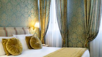 A hotel room with a bed, pillows, a nightstand, a lamp, and curtains.