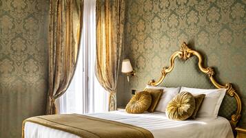 A classic, elegantly furnished bedroom with a large bed, ornate headboard, and patterned wallpaper.