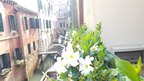 A narrow canal with buildings on either side, a bridge, and a balcony with white flowers. - Hotel Locanda Canal (Venice)