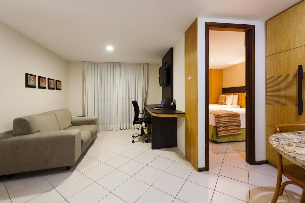 Una habitación de hotel con sofá, escritorio, televisor, cama y mesa de comedor.
