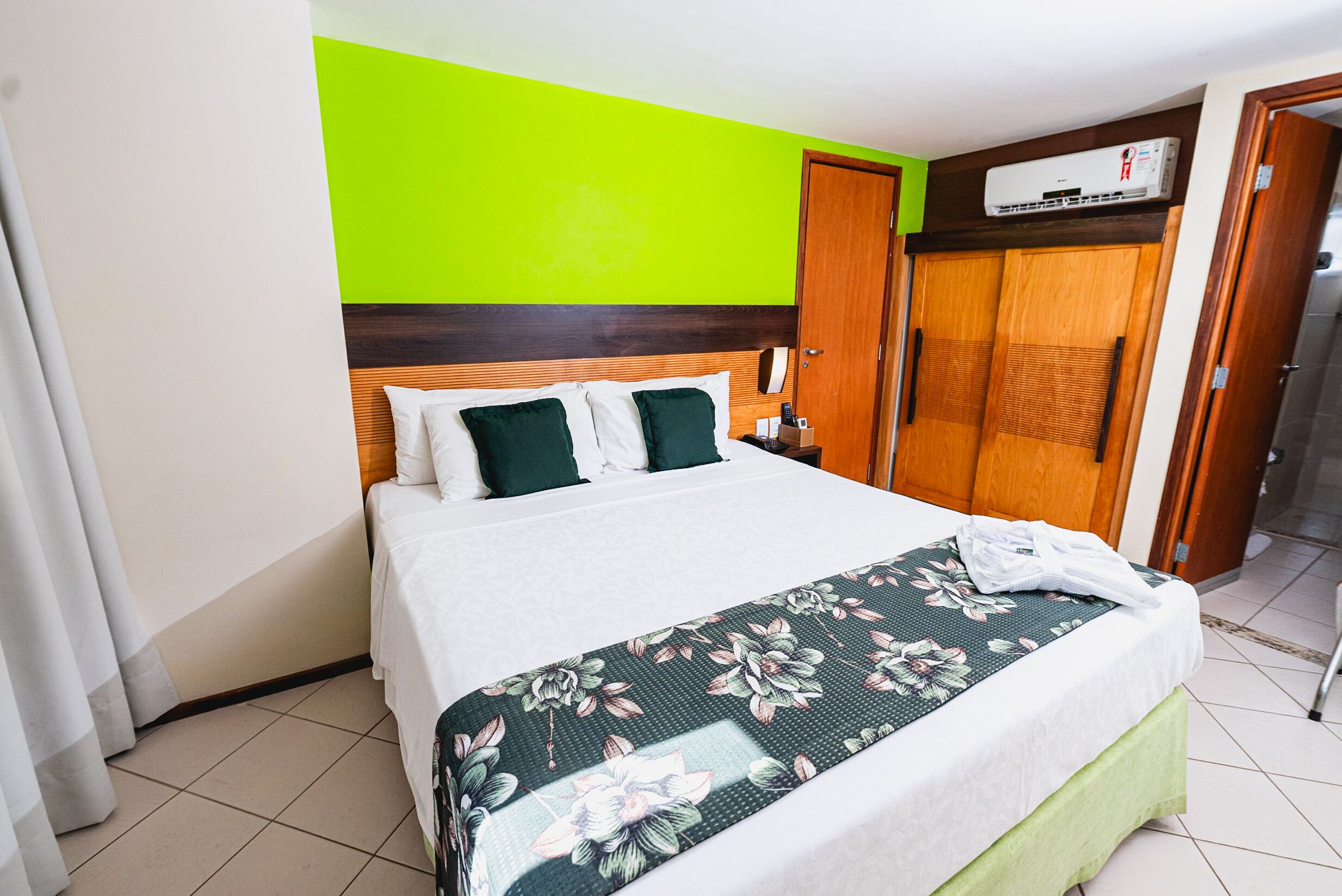 Habitación de hotel con una cama, pared verde, armario de madera y suelo de baldosas.