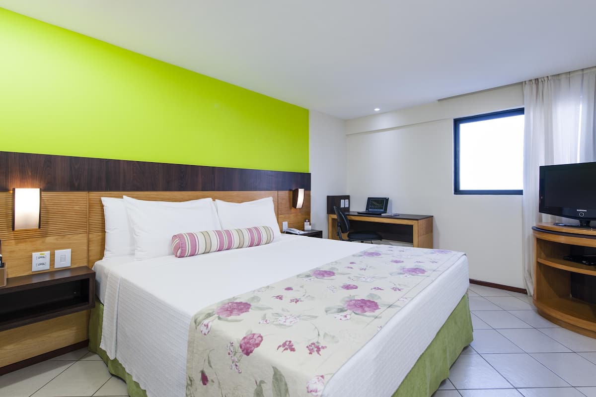Una habitación de hotel con cama, escritorio, televisor y ventana.