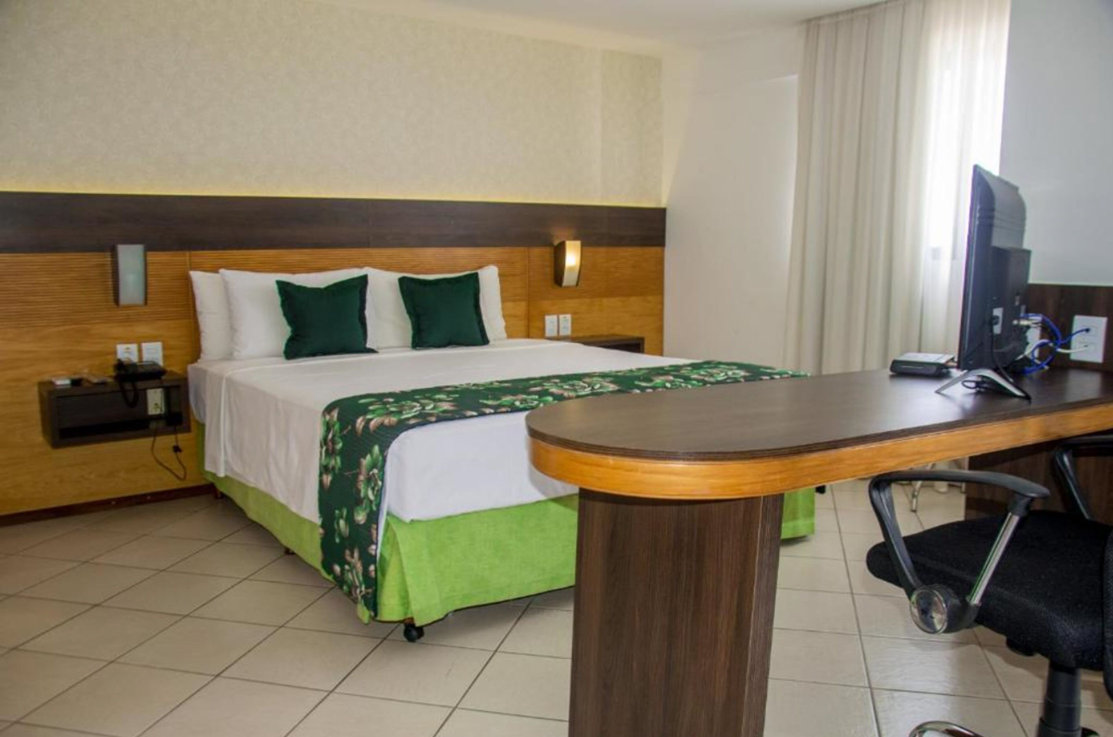 A hotel room with a bed, a desk, a chair, a TV, and a window with curtains.