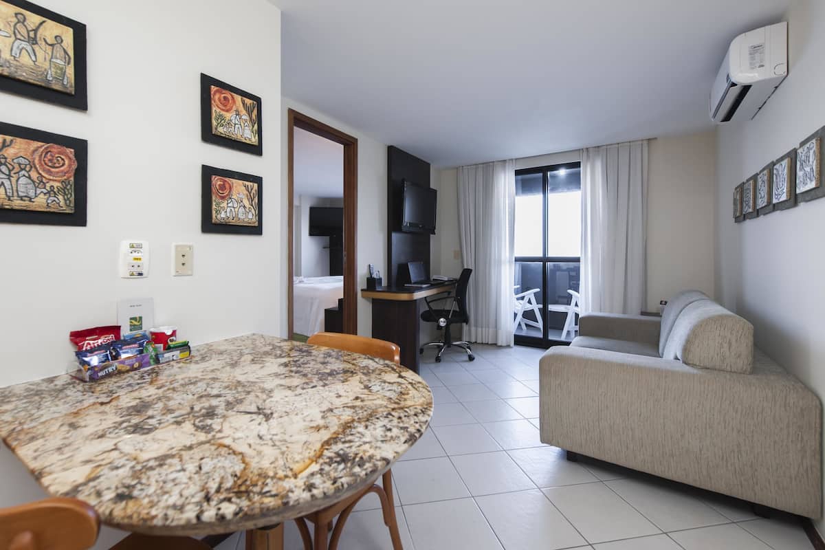 Una habitación de hotel con una mesa de comedor, un sofá, un televisor y obras de arte en las paredes.
