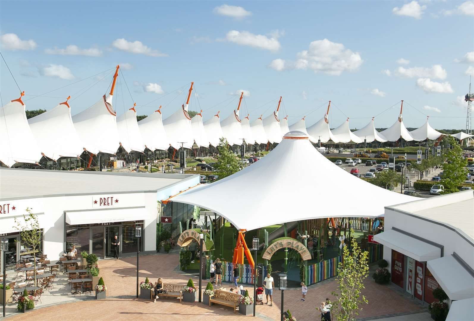Een modern winkelgebied met een opvallende witte tentconstructie, terrasplekken en een zichtbare Pret winkel.