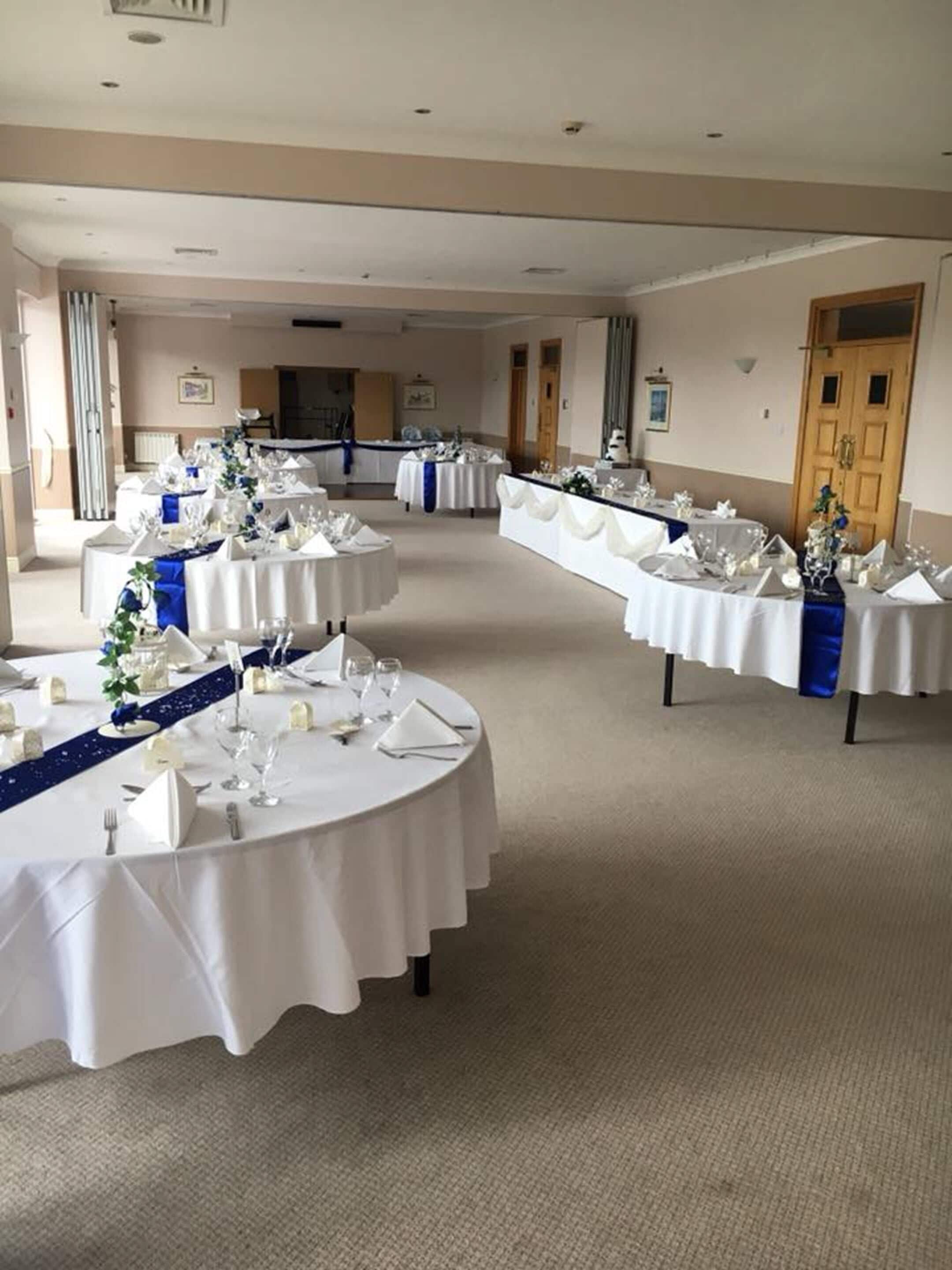 Une salle de banquet avec des tables rondes dressées pour un événement formel, agrémentée de nappes blanches et de rubans bleus.