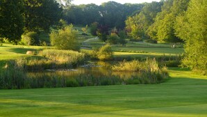 A golf course with a pond, surrounded by trees and grassy areas. - London Beach Country Hotel (Tenterden)