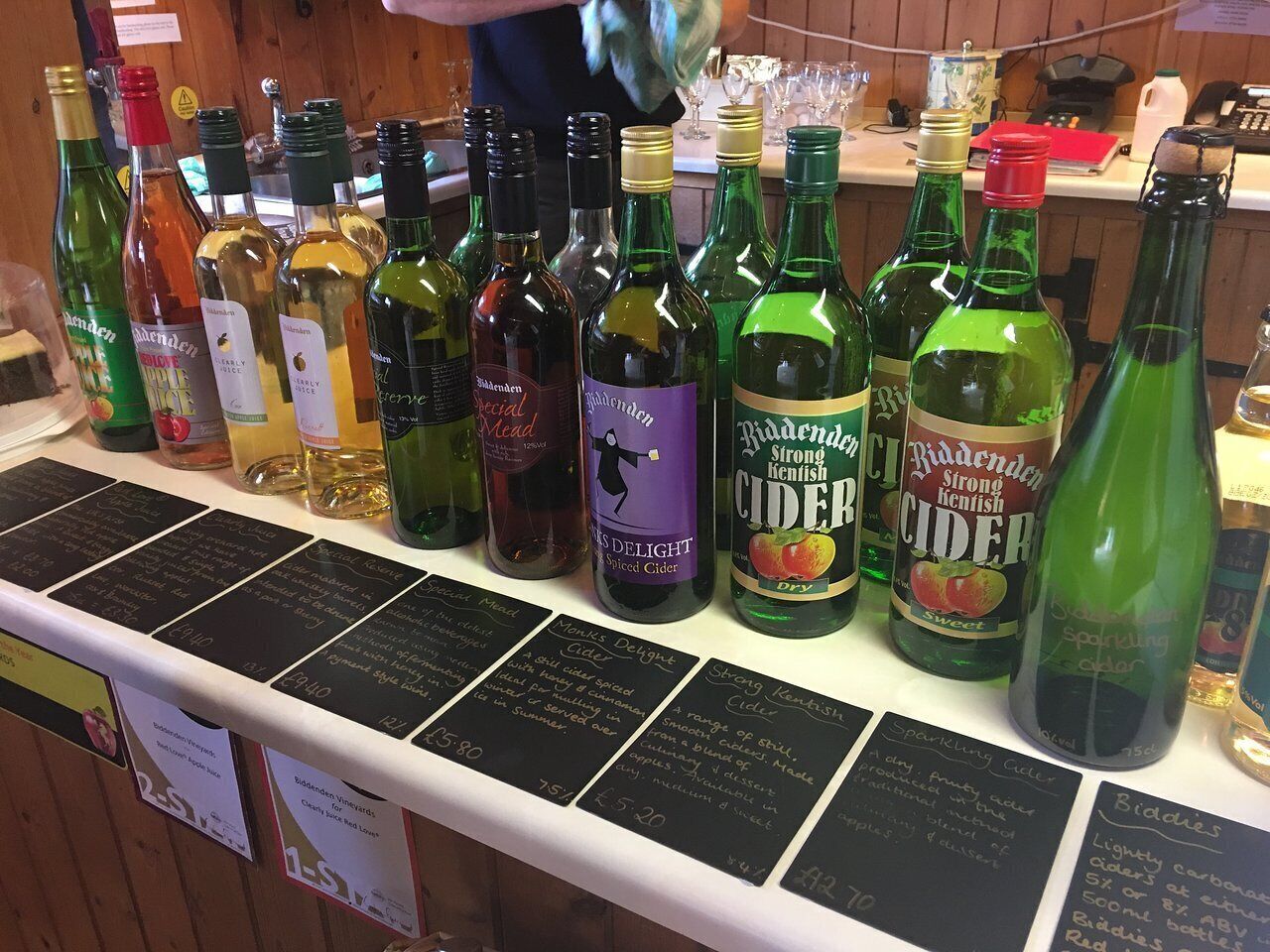 Variedad de botellas de sidra sobre una barra con etiquetas y precios.