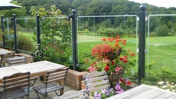An outdoor patio with wooden tables and benches, surrounded by a metal fence and a flower bed with red and pink flowers. - London Beach Country Hotel (Tenterden)