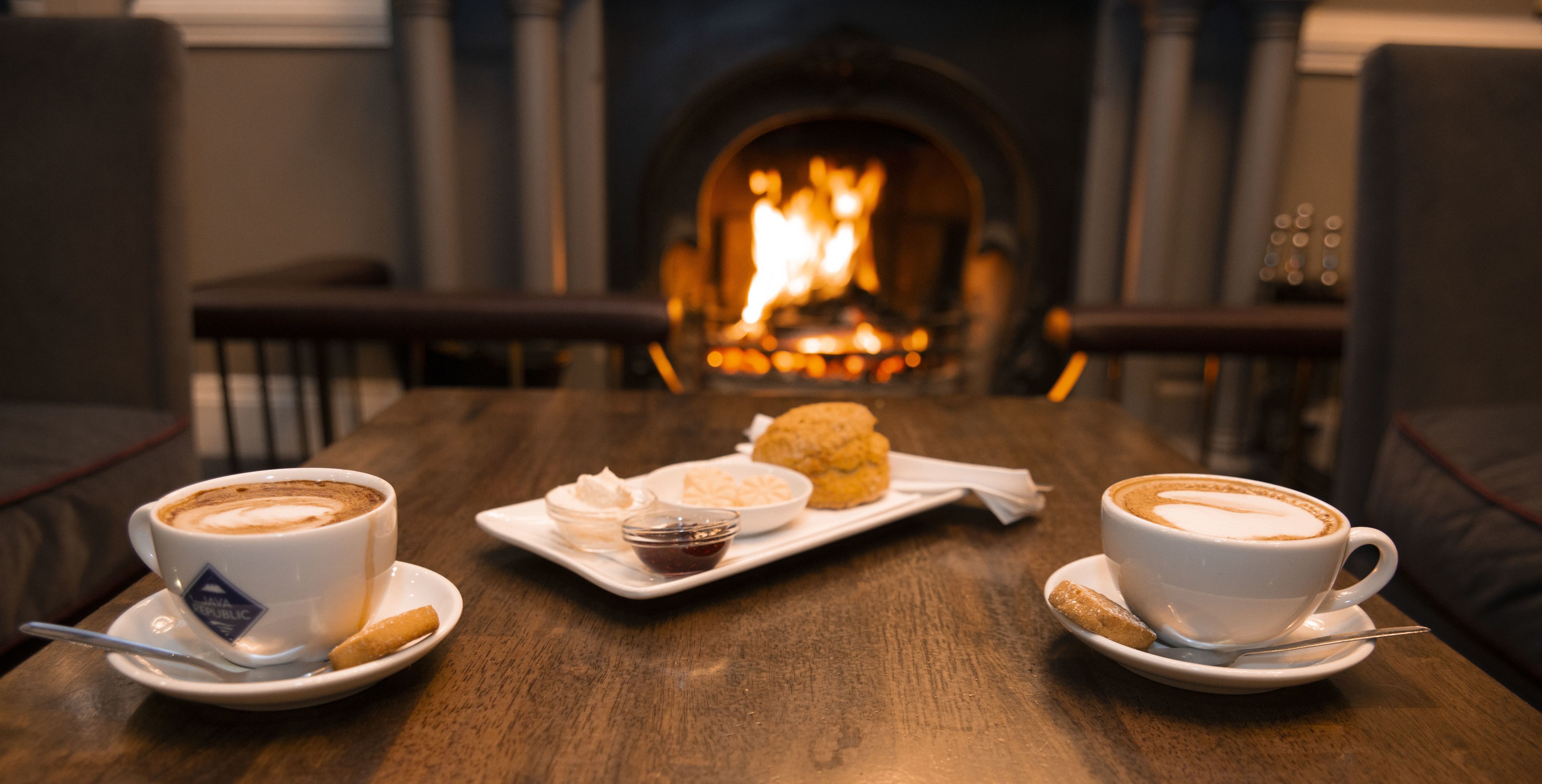 A table with two cups of coffee, a plate with pastries, and a small bowl of jam.