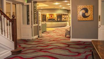 Un hall de hotel con mostrador de recepción, una escalera y una alfombra estampada.