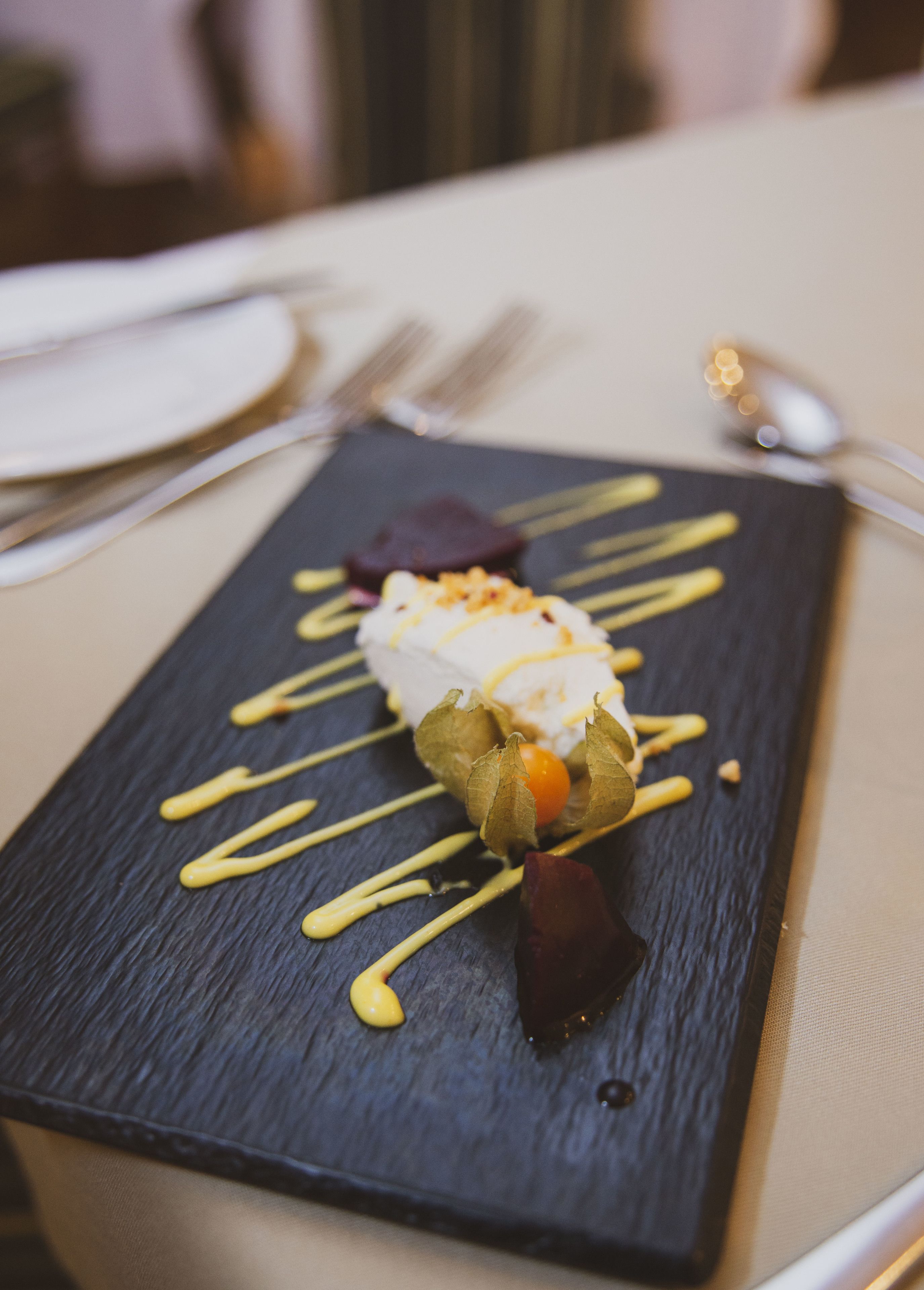 A dessert on a slate plate with drizzles of sauce and garnishes.
