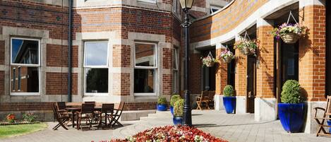 A brick building with a curved facade, outdoor seating, and flower beds.