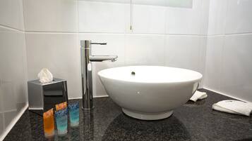 A bathroom with a white sink, a mirror, and a towel rack. There are three bottles of hand soap on the counter.