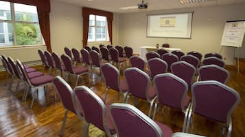 Une salle de conférence avec des rangées de chaises violettes, un écran de projection et un tableau blanc.