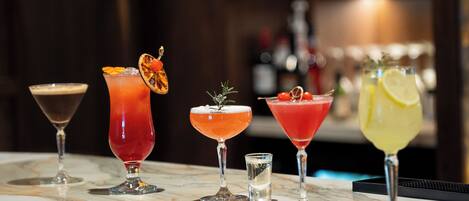 A bar counter with five different cocktails, each with unique garnishes.