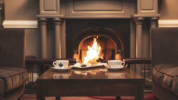 A cozy room with a fireplace, a table with a tray of cookies and cups, and two chairs.