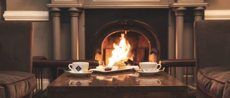 A cozy room with a fireplace, a table with a tray of cookies and cups, and two chairs.