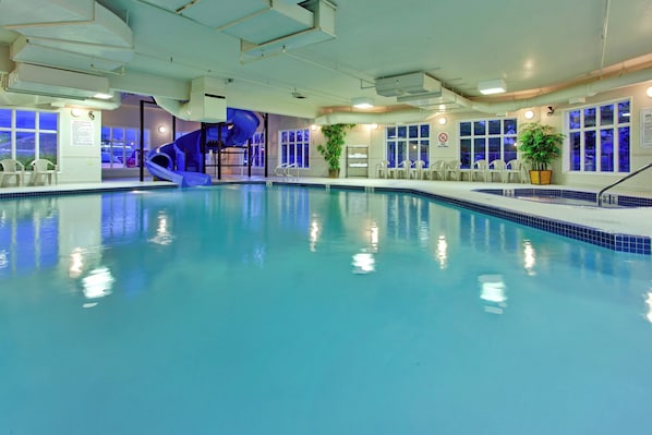 An indoor swimming pool with a blue slide, seating area, and a no diving sign.