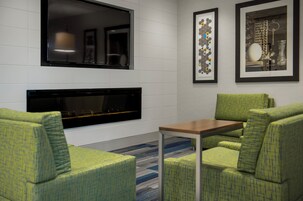 Un área de descanso moderna con chimenea, sillones estampados en tonos verdes, una mesita y cuadros enmarcados en la pared.