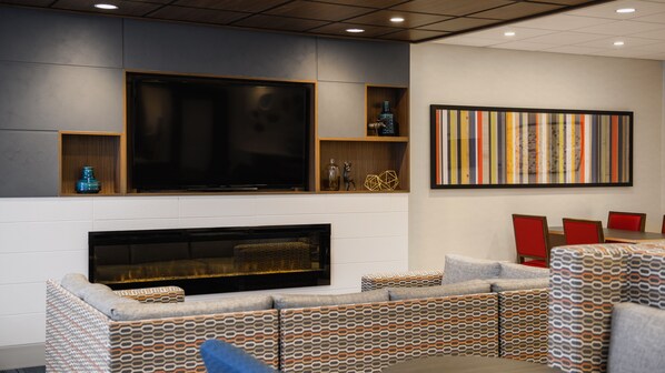 A modern living room with a fireplace, a flat-screen TV, and a colorful abstract painting. - Holiday Inn Express Hotel & Suites Airdrie-Calgary North by IHG (Airdrie)
