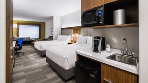 A hotel room with two beds, a microwave, a coffee maker, a sink, and a desk with a chair.