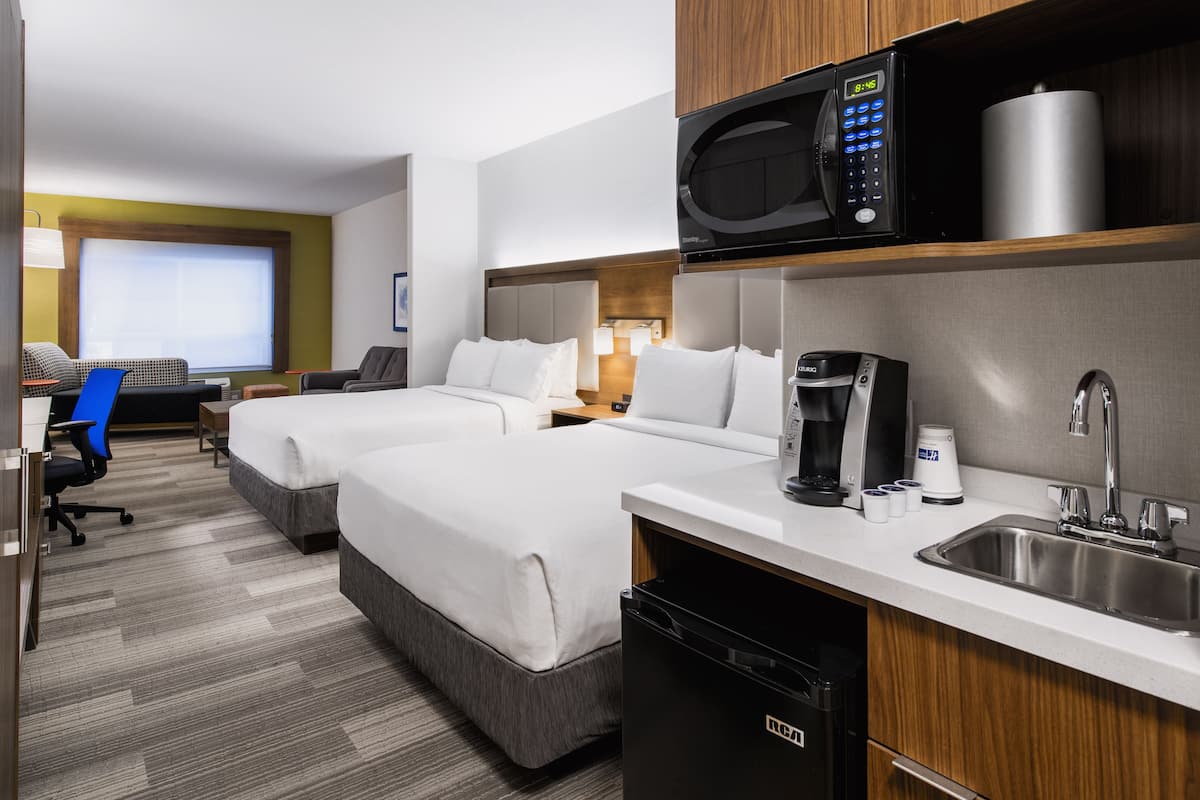 A hotel room with two beds, a microwave, a coffee maker, a sink, and a desk with a chair.