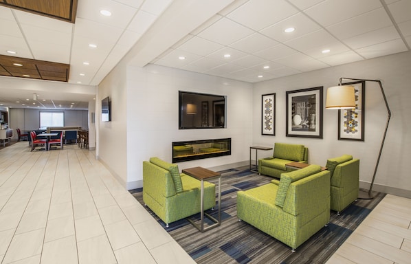 Eine moderne Hotelhalle mit grĂĽnen, gepolsterten Sofas, einem Flachbildfernseher, gerahmten Kunstwerken und einem gemusterten Teppich.