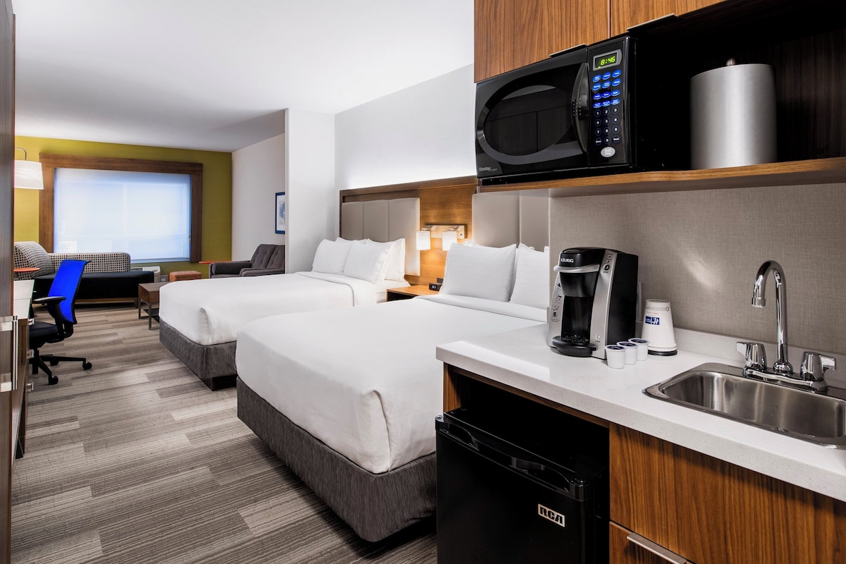 Een hotelkamer met twee bedden, een magnetron, een koffiezetapparaat, een wastafel en een bureau met een stoel.