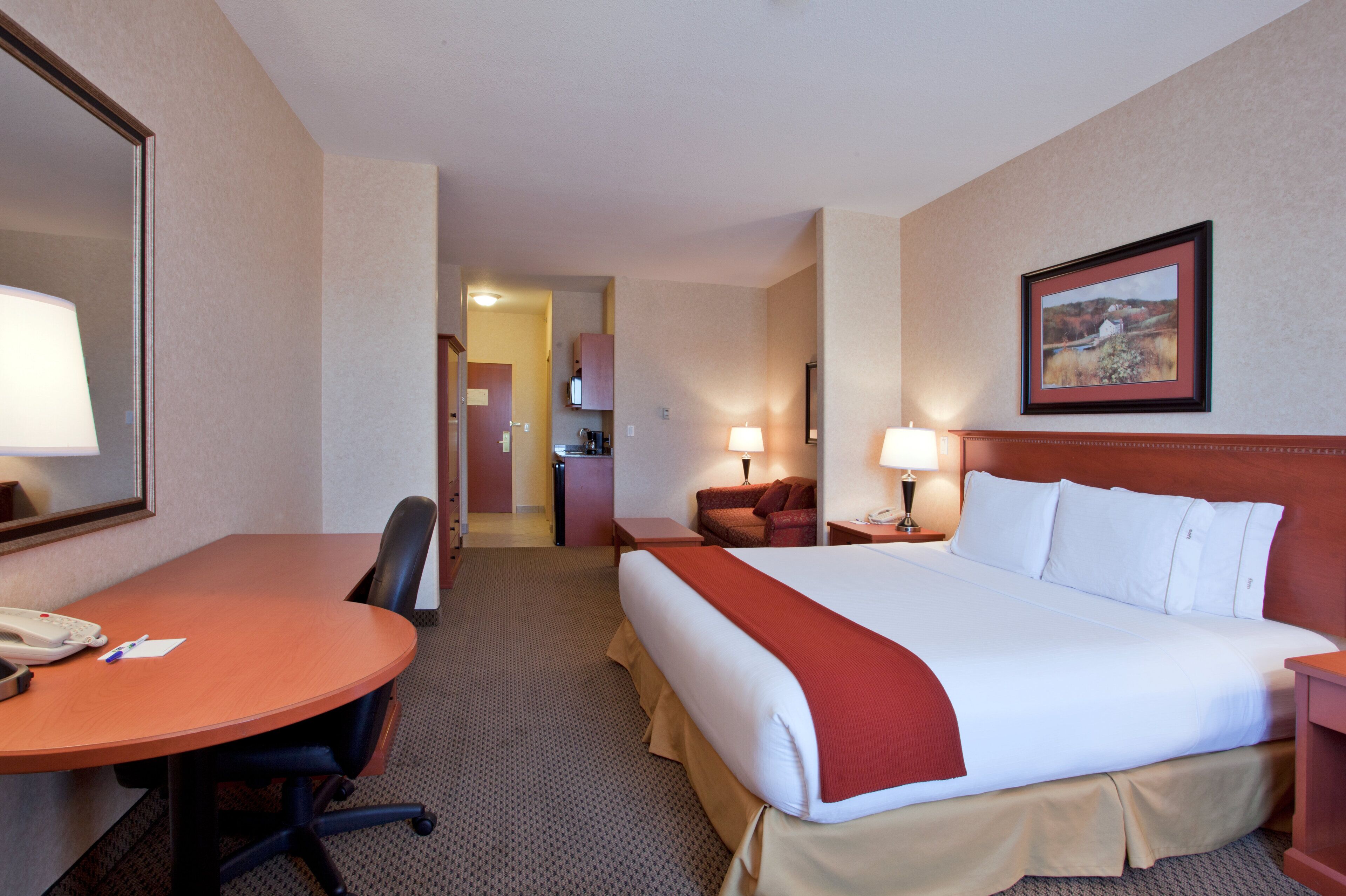 Een hotelkamer met een bed, een bureau, een stoel, een telefoon, een lamp en een schilderij aan de muur.